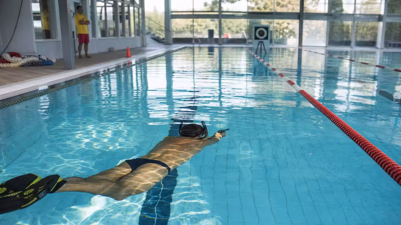 Pratiquant équipé de palmes visant une cible subaquatique dans un couloir de piscine réservé et surveillé