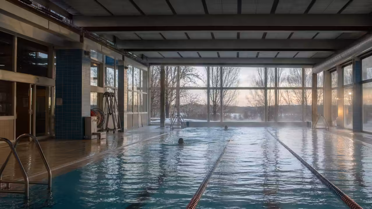 Bassin municipal chauffé en hiver, eau calme et éclairage intérieur visible derrière de larges baies vitrées