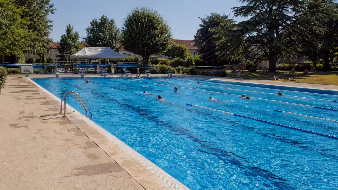 Bassin extérieur de 25 mètres avec lignes d’eau, pataugeoire et plage minérale sous le soleil d’été