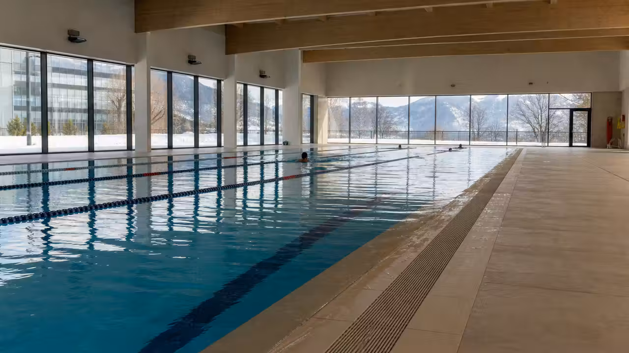 Bassin municipal intérieur rénové avec lignes d’eau, carrelage clair et lumière d’hiver entrant par les baies