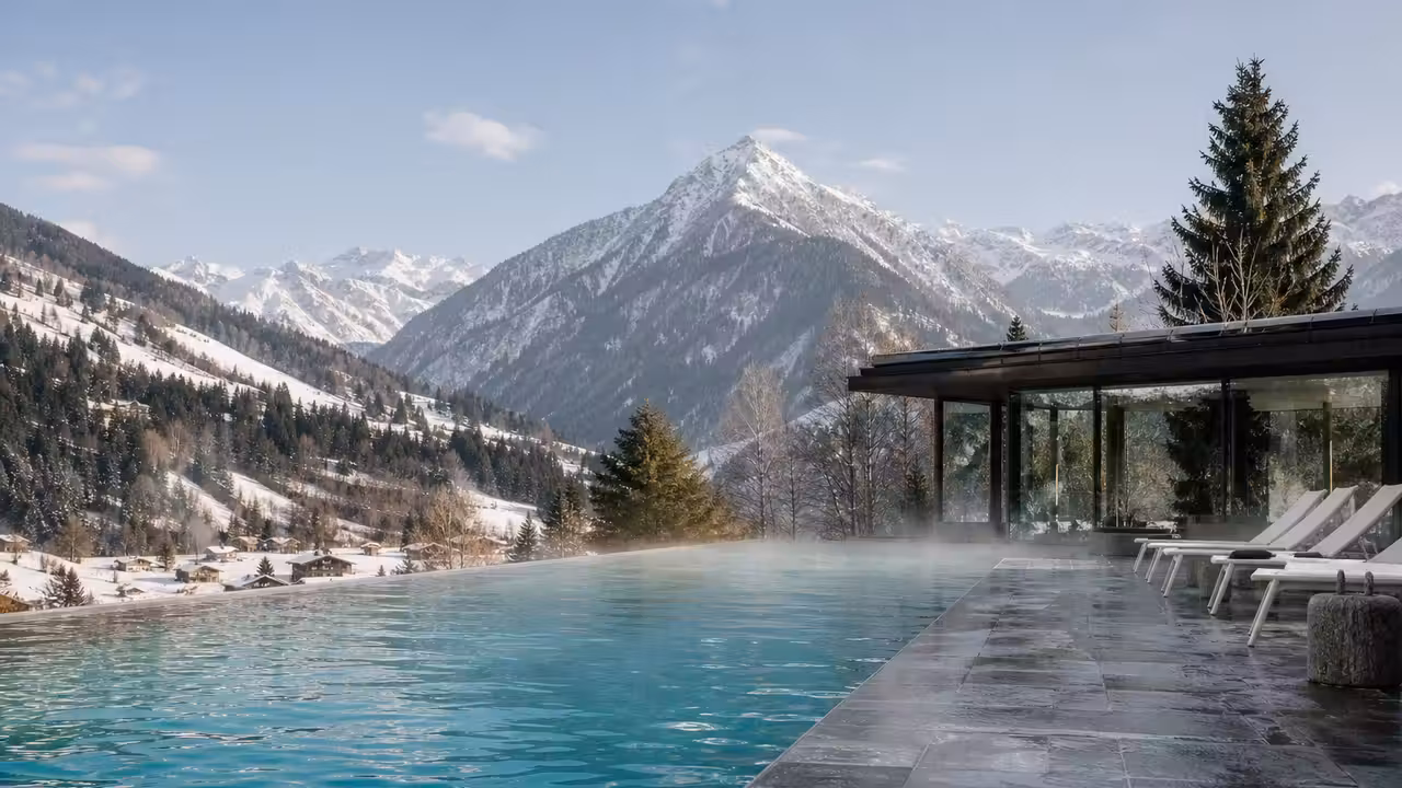Bassin extérieur fumant au pied de montagnes enneigées, relié à un espace de spa vitré