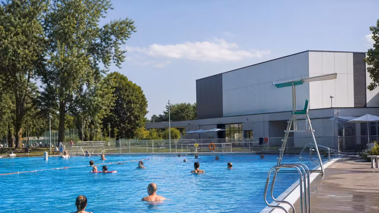 Bassin extérieur d’une piscine municipale avec nageurs, lignes d’eau et locaux techniques en arrière-plan