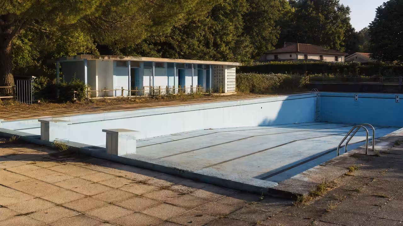 Ancien bassin extérieur vide entouré de gradins et de végétation dans un équipement municipal français