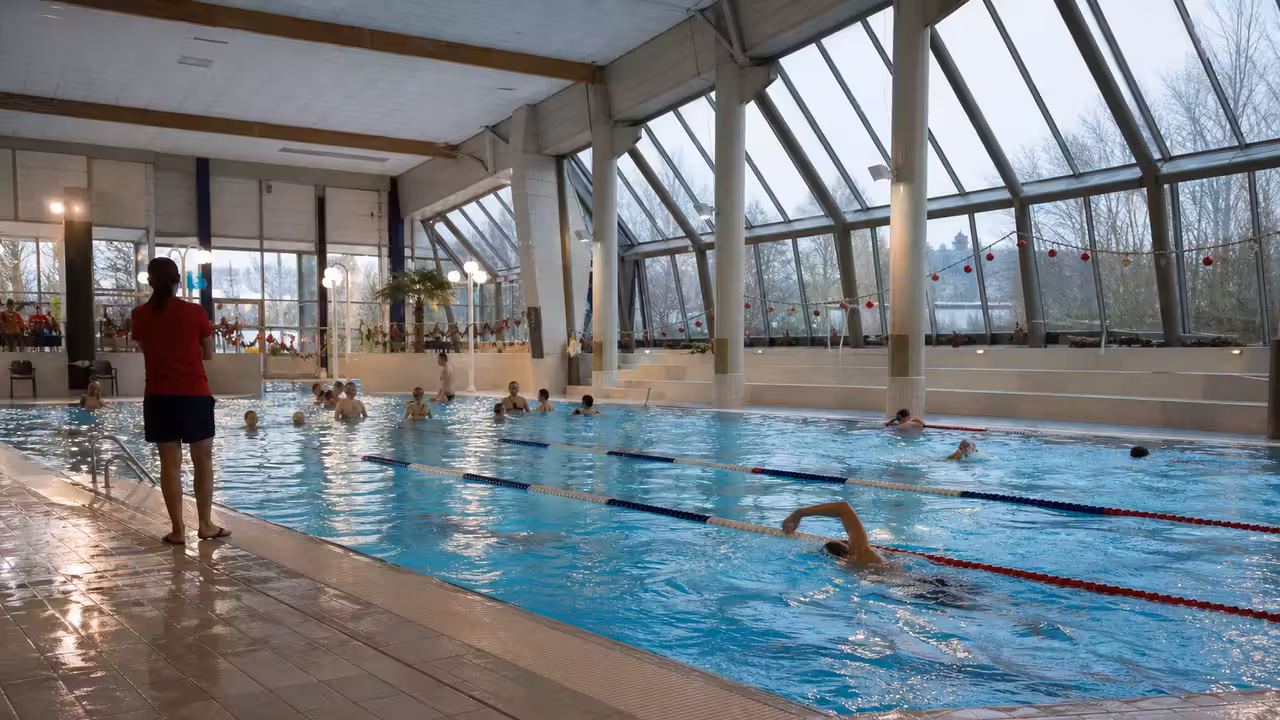 Nageurs et familles dans le bassin couvert lumineux d’une piscine publique française pendant les vacances d’hiver