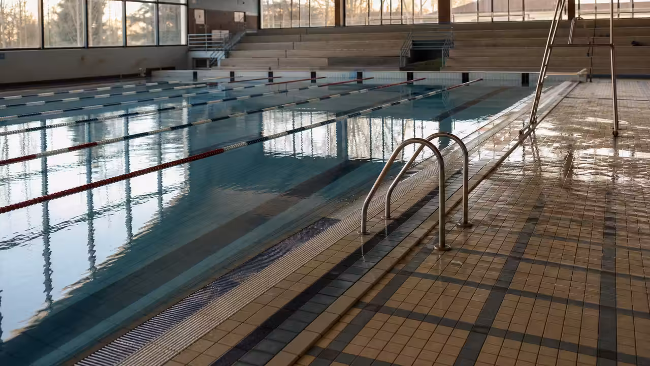 Bassin intérieur de piscine municipale vide, lignes d’eau et lumière naturelle avant une fermeture