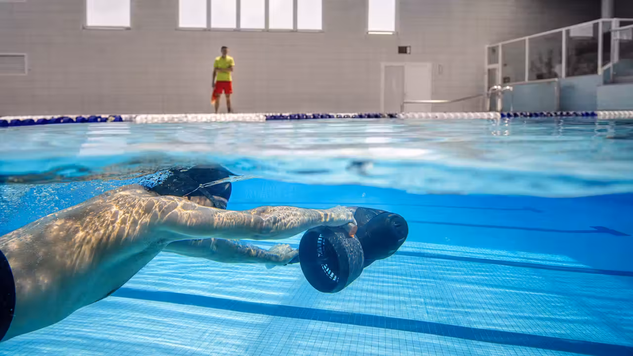 Scooter sous-marin tenu par un nageur dans une ligne d’eau réservée d’une piscine couverte