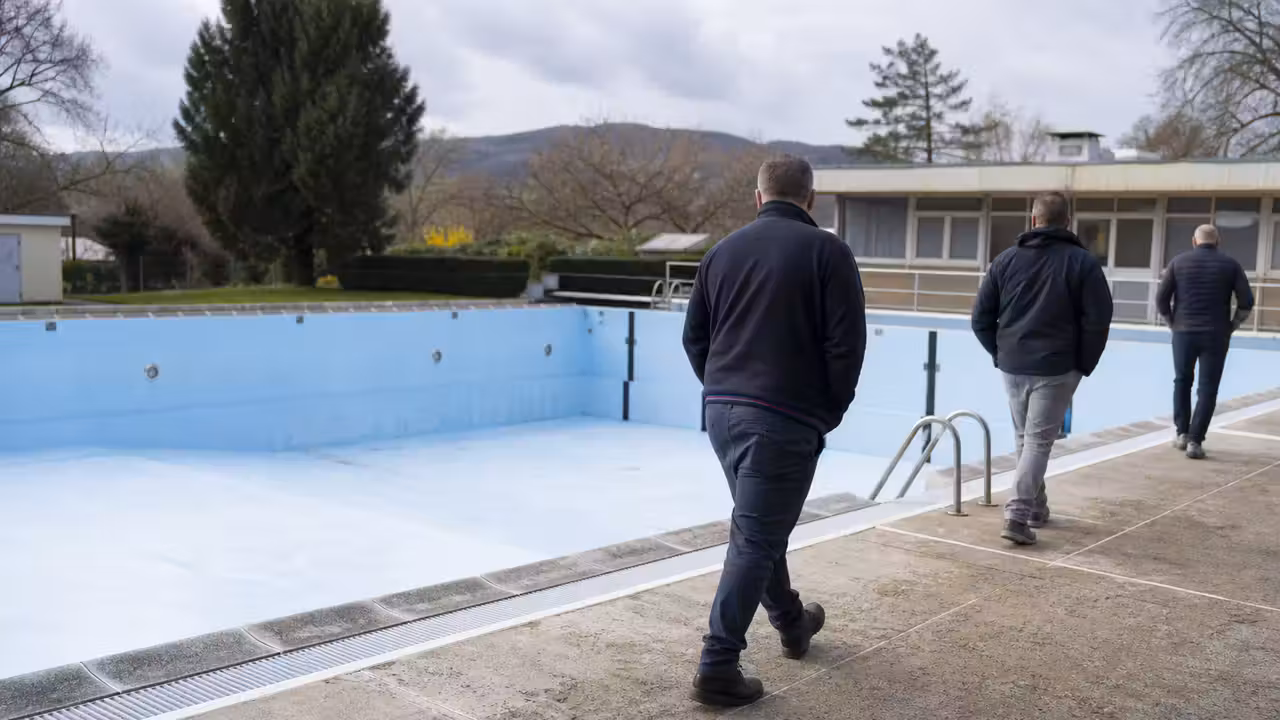 Piscine municipale de plein air vide en début de saison, avec bassin et plages minérales à rénover