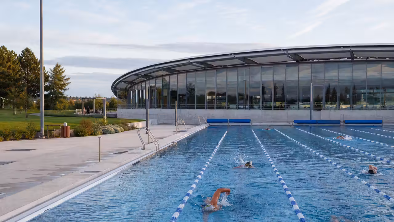 Bassin municipal extérieur de 50 mètres avec lignes de nage, espace vert et halle aquatique en arrière-plan