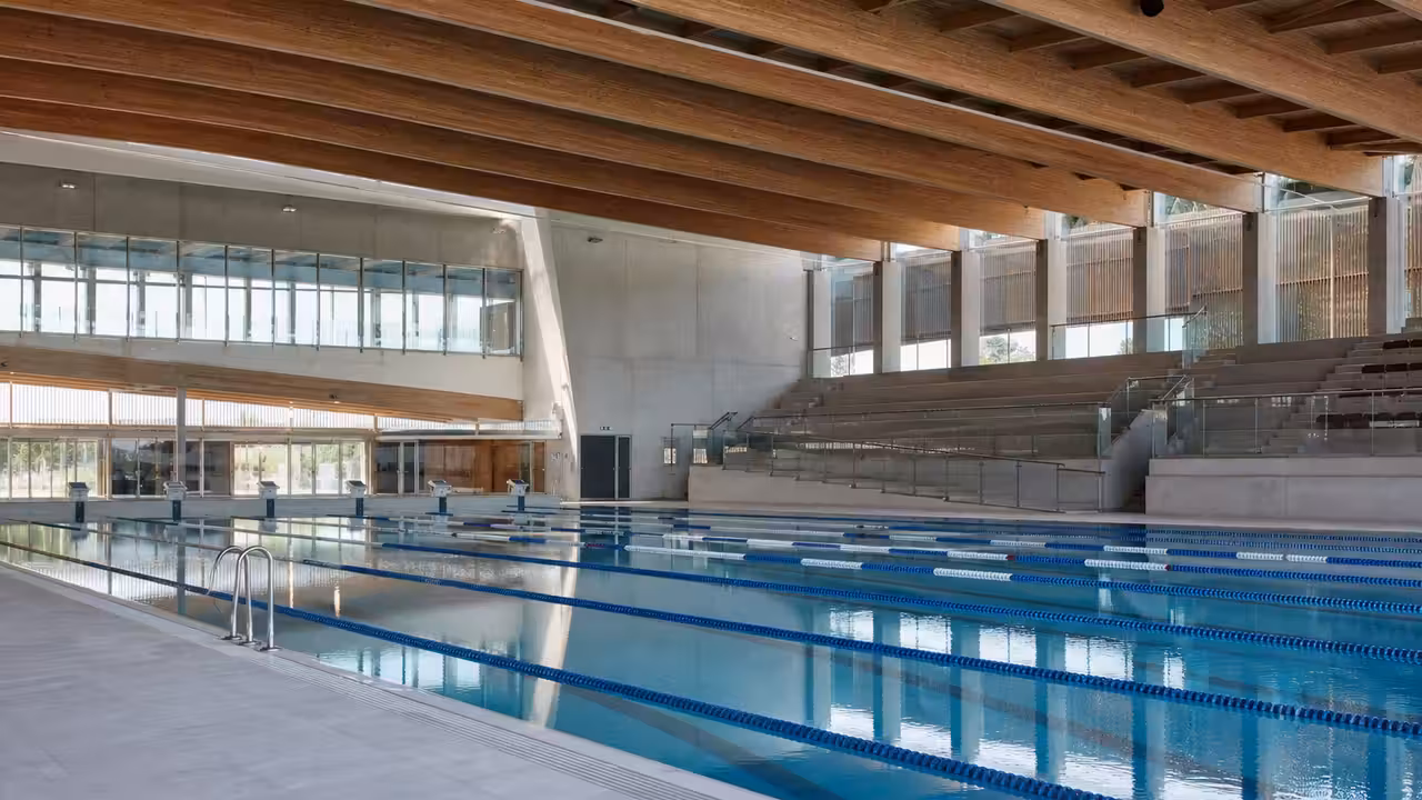 Vue intérieure d’un grand bassin de natation vide, avec lignes d’eau et baies vitrées lumineuses