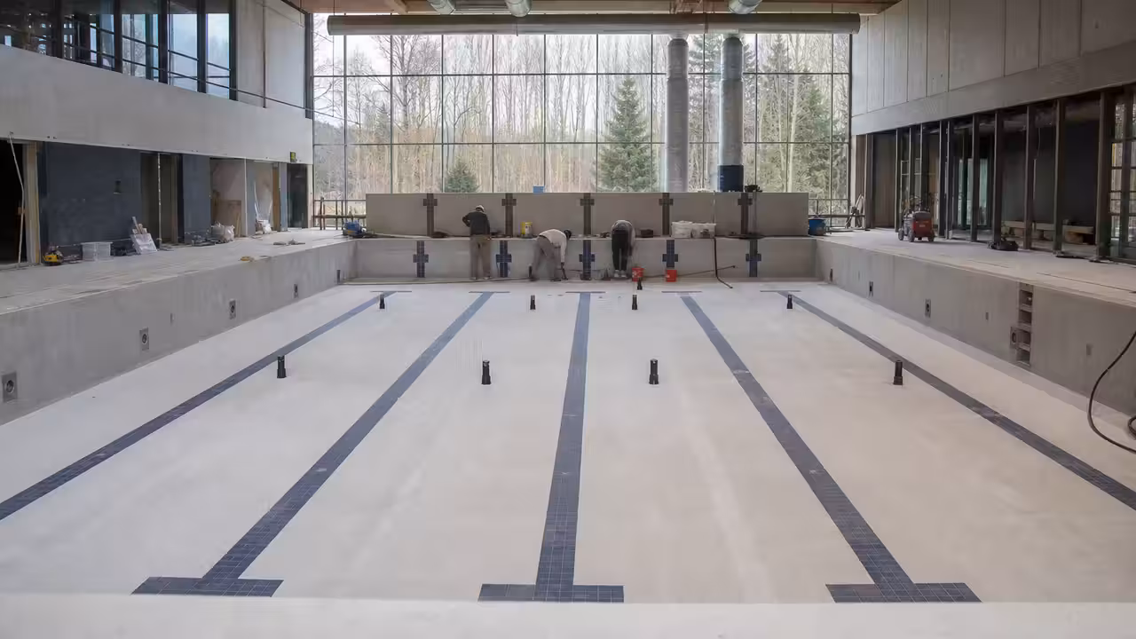 Bassin public couvert moderne avec lignes de nage, baies vitrées et espaces techniques en arrière-plan