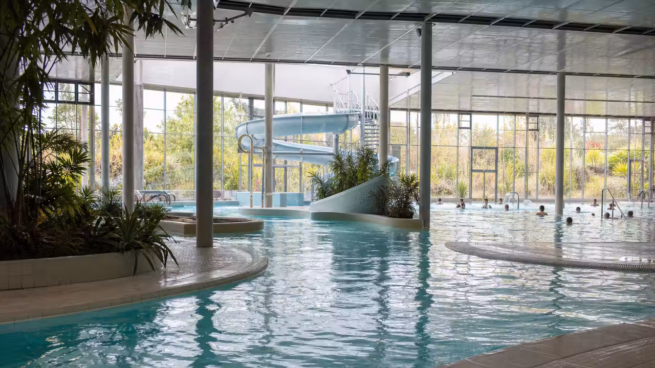Bassin couvert contemporain avec toboggan, plages antidérapantes et lumière naturelle dans un centre aquatique