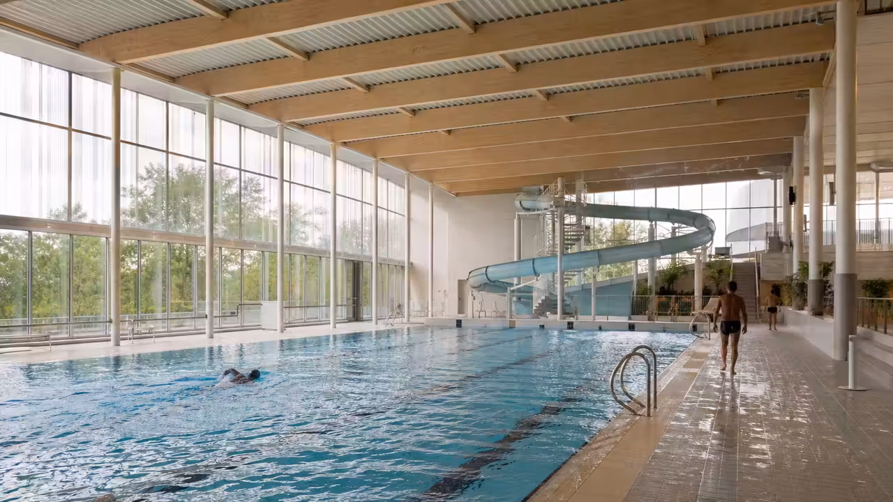 Bassin sportif lumineux d’un centre aquatique moderne avec toboggan intérieur et espaces de baignade