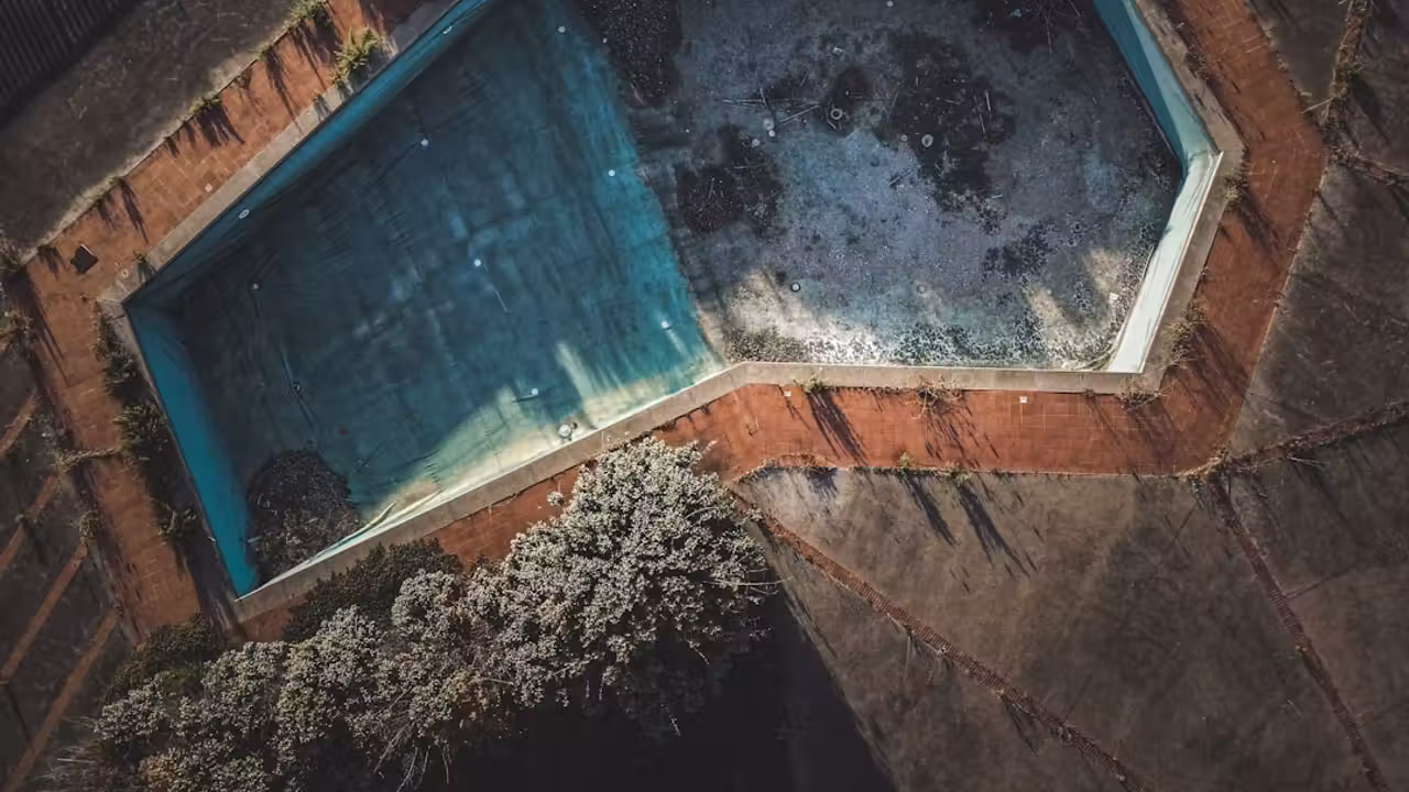 Bassin de baignade urbain installé sous un pont ferroviaire, avec plages minérales et lumière naturelle latérale
