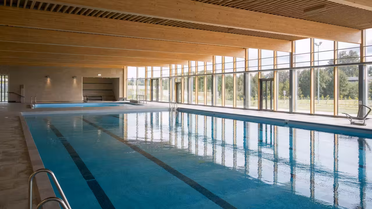 Bassin intérieur lumineux avec couloirs de nage, baies vitrées et vestiaires d’un équipement municipal moderne