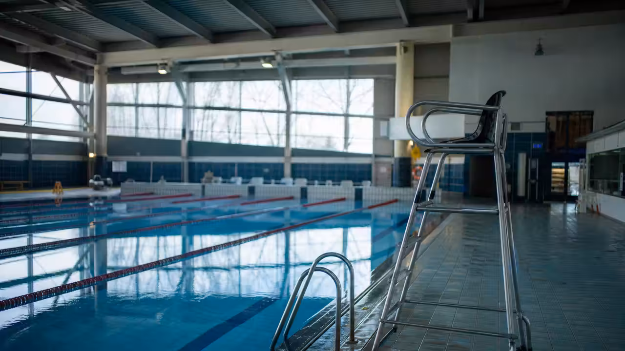 Bassin intérieur d’une piscine municipale vide, avec chaise de surveillance inoccupée au bord de l’eau