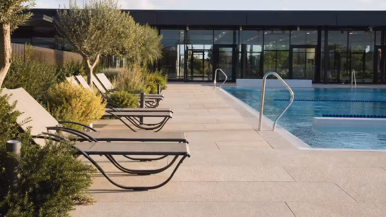 Vue d'ensemble d'un solarium paysager avec transats au bord d'une piscine municipale contemporaine