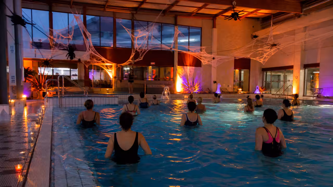Animation aquagym en soirée dans une piscine publique décorée pour Halloween, avec éclairage coloré