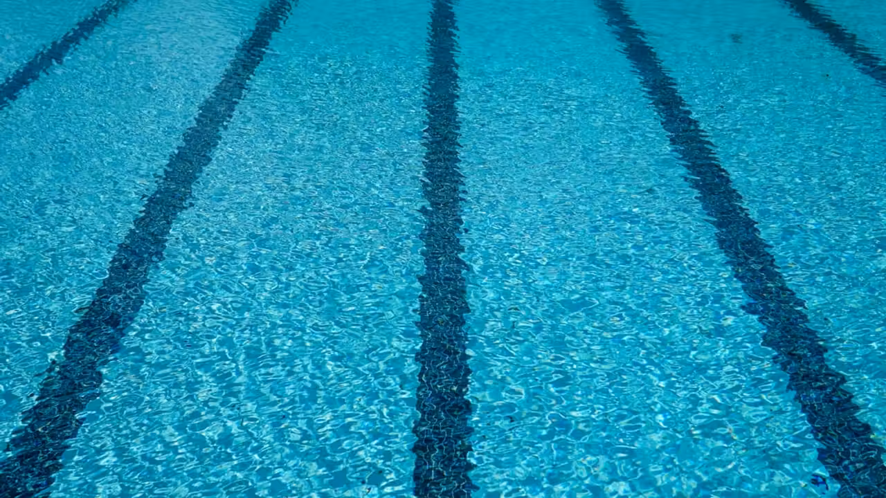 Bassin extérieur de piscine municipale avec lignes d’eau, plage minérale et collines des Hautes-Pyrénées
