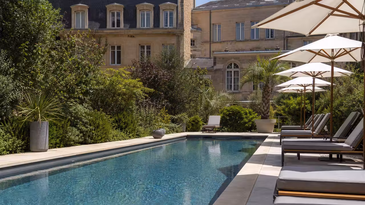 Piscine extérieure rénovée au cœur d’une résidence urbaine, avec plage minérale, transats et végétation