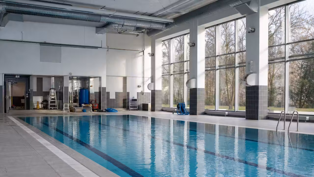 Hall de piscine publique couvert avec bassin calme, baies vitrées et réseaux de ventilation au plafond