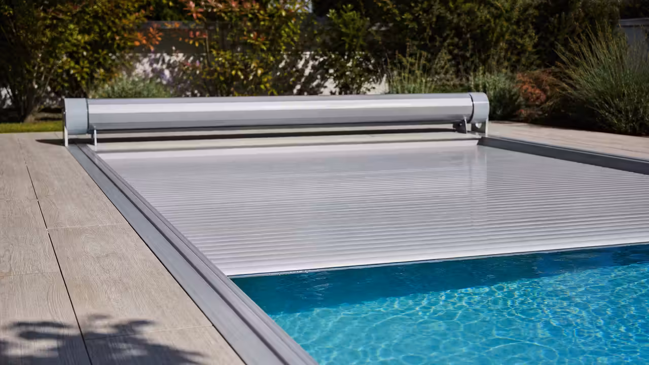Volet roulant de piscine à moitié déployé sur un bassin, lames PVC et glissières latérales visibles