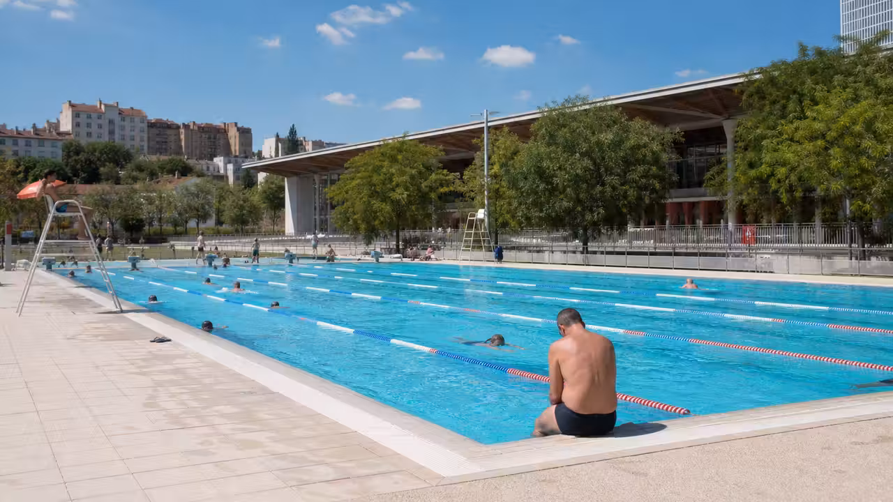Bassin extérieur municipal à Lyon avec nageurs au loin et plages minérales baignées de soleil