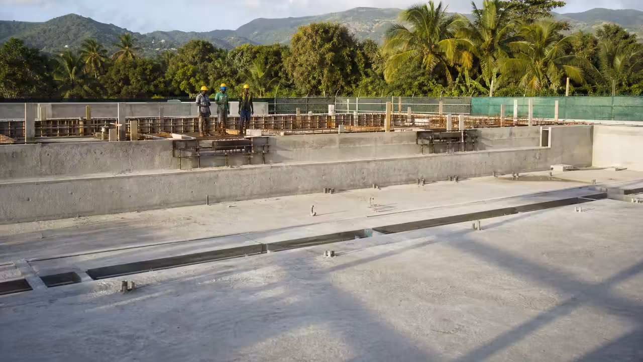 Bassin de natation en construction dans un environnement tropical, avec structures métalliques et ouvriers au travail